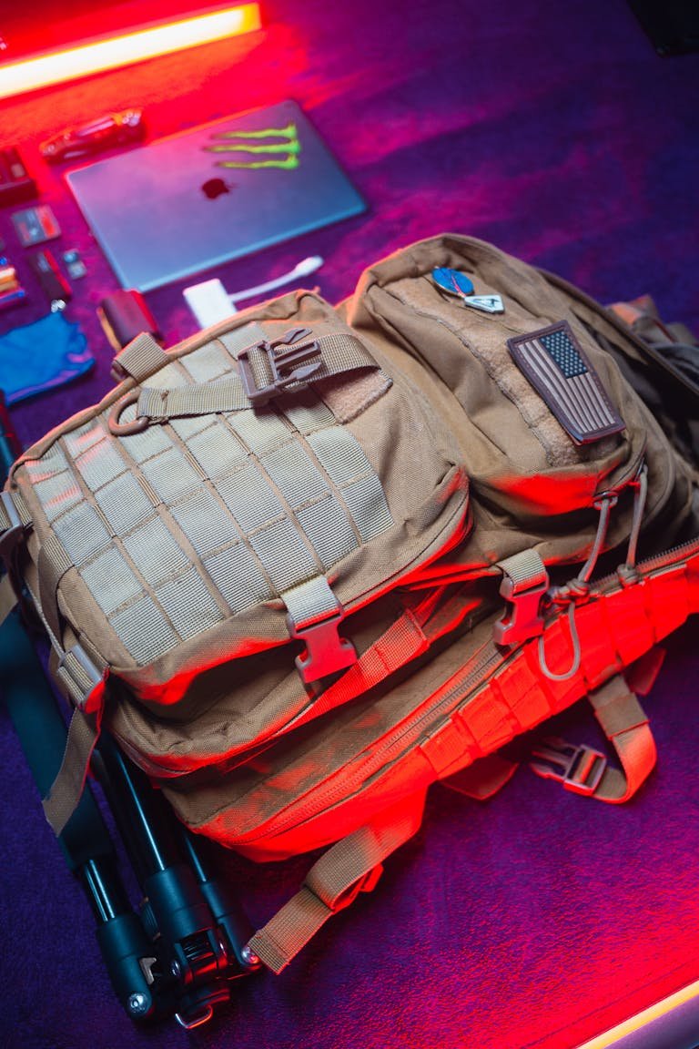 An overhead view of a tactical backpack and camera equipment illuminated by colorful lights.